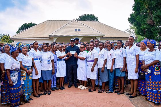 Wide view of Peter Obi presenting a cheque to hospital staff in a courtyard lined with women in blue and white