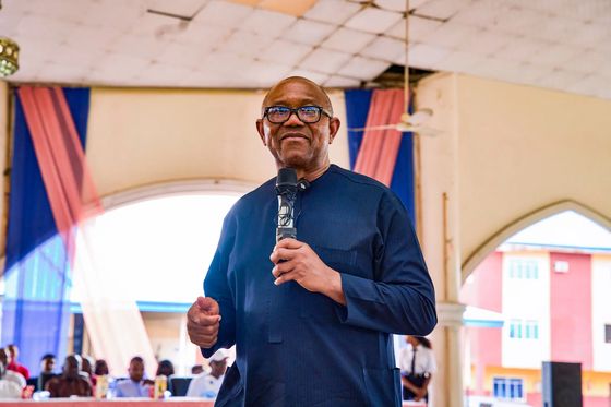 Peter Obi speaking into a handheld microphone under an arched hall roof
