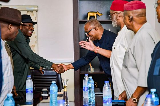 Peter Obi bowing slightly to shake hands across a table, elders in red caps looking on
