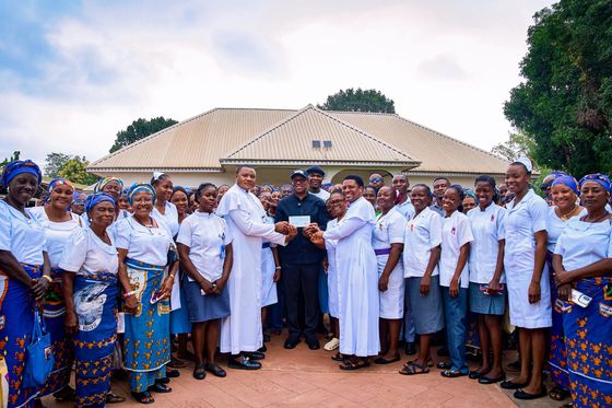Peter Obi presenting a cheque in a paved courtyard flanked by two rows of women in blue and white