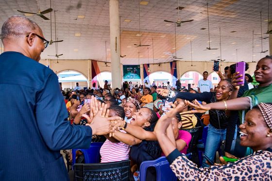 Peter Obi leaning across a barrier to touch the hands of a crowd of young women in a hall