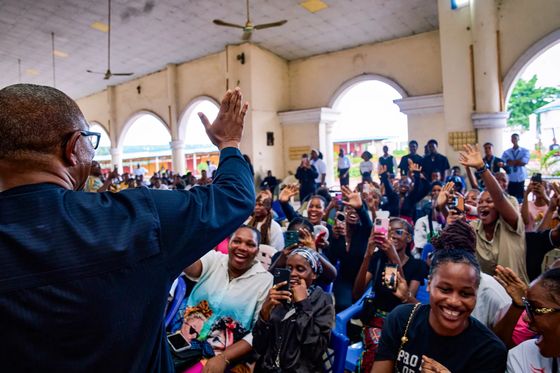 Peter Obi photographed from behind with his hand raised to a hall full of women and young people