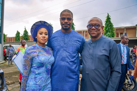 Peter Obi standing outside a building with a woman in a blue gele and a man holding a folder