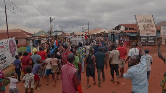 A street packed with people, hands and phones raised, as a vehicle moves slowly through